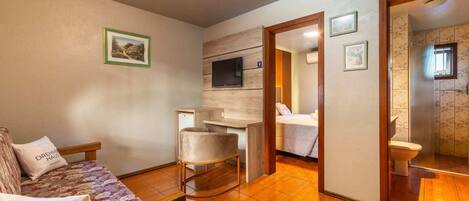 A compact living space with a sofa, a small table, a TV, and a bathroom visible through an open door.