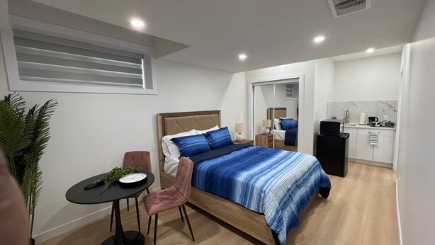 Ein modernes Schlafzimmer mit Bett, Nachttischen, Schreibtisch und Stuhl. Es gibt eine kleine Küchenzeile mit Spüle und Herd.
