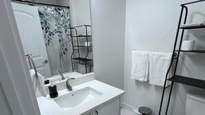 Ein modernes Badezimmer mit einem weißen Waschbecken, einem Spiegel, einer Toilette und einem Regal mit Handtüchern.