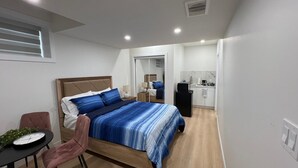 Ein modernes Schlafzimmer mit einem großen Bett, Nachttischen, einem kleinen Schreibtisch und einer Küchenzeile.