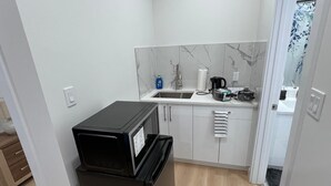 Eine kleine Küche mit weißen Schränken, einem schwarzen Kühlschrank, einer Spüle und einer Arbeitsplatte mit verschiedenen Geräten.