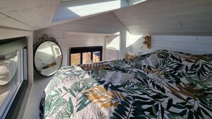Un dormitorio con tragaluz, una cama con colcha de estampado de hojas, un espejo redondo y un adorno de pared de madera.