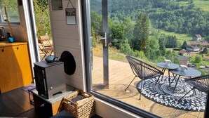 Una habitación con un ventanal grande que da a un paisaje pintoresco, una pequeña mesa con sillas y un armario de madera.