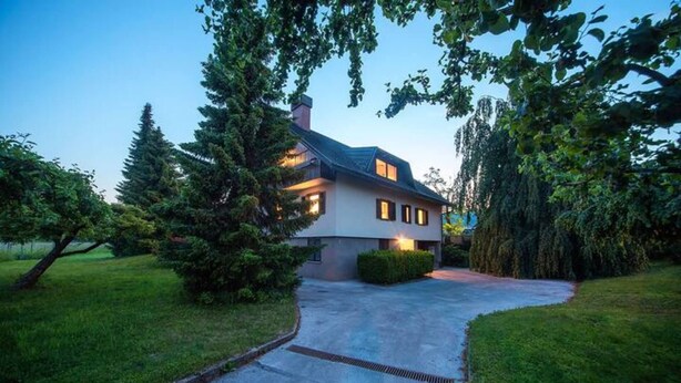 A two-story house with a driveway leading to the entrance, surrounded by trees and a well-maintained lawn.