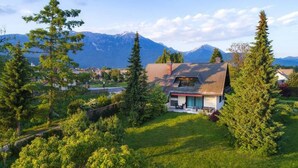 A house with a sloped roof, surrounded by lush greenery and mountains in the background.
