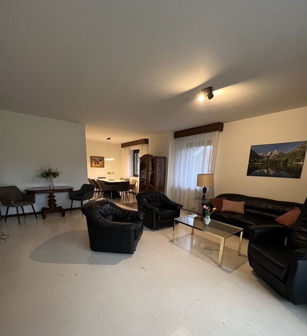 A living room with a dining area, a sofa, armchairs, a coffee table, and a painting on the wall.