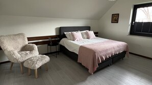 A bedroom with a bed, a chair, a bedside table, and a window.