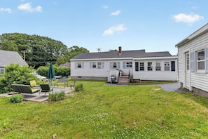 A two-story house with a front porch, a small attached garage, and a backyard with a lawn and patio furniture.