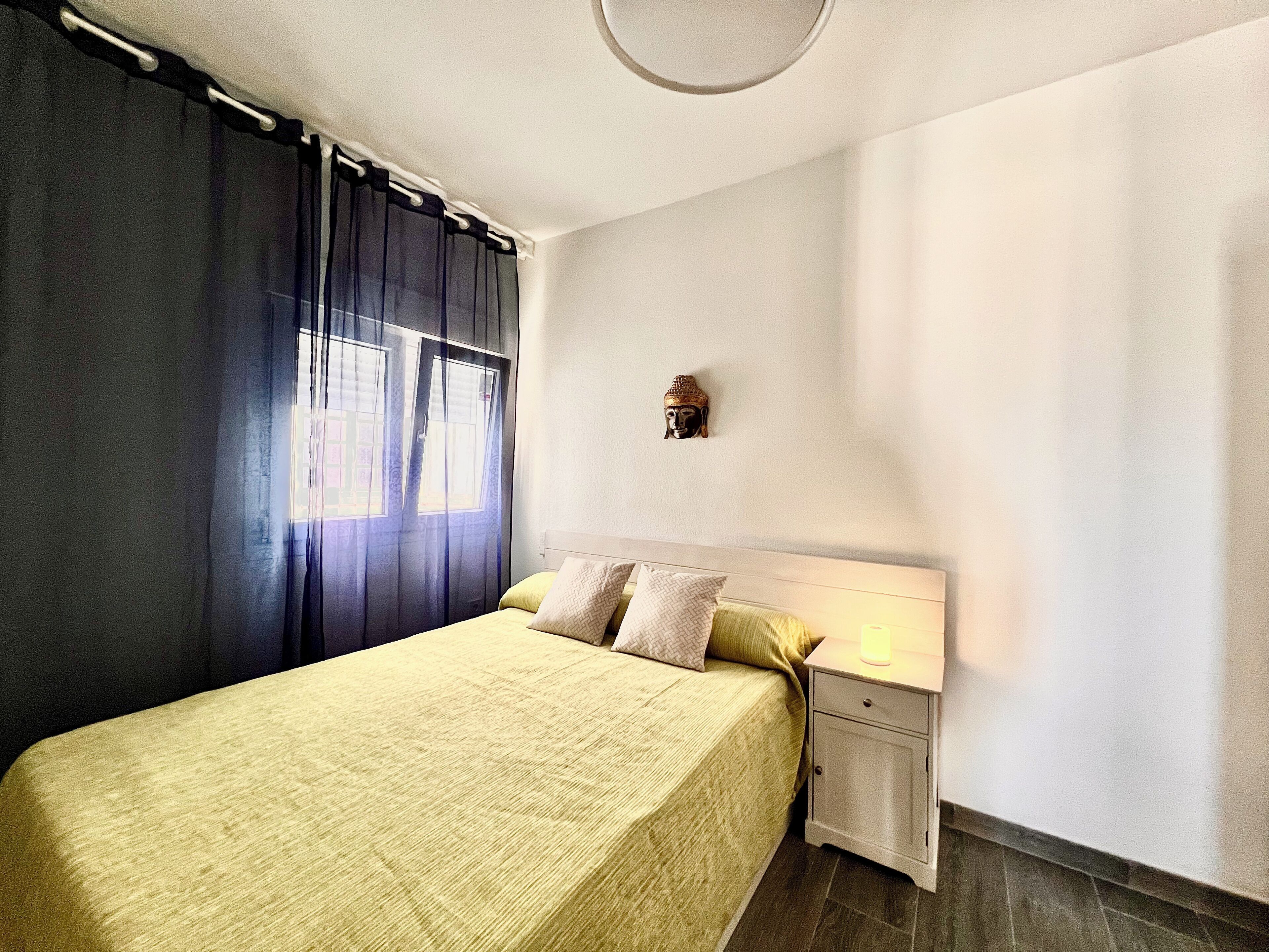 A bedroom with a bed, nightstand, and a Buddha statue on the wall.