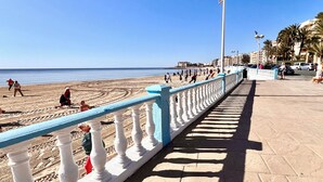 A coastal promenade with a tiled walkway, a blue railing, and a clear view of the beach and ocean.