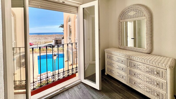 A room with a balcony, a pool, and a wicker console.