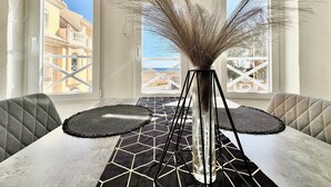 A dining area with a table, chairs, and a tall vase with dried plants.