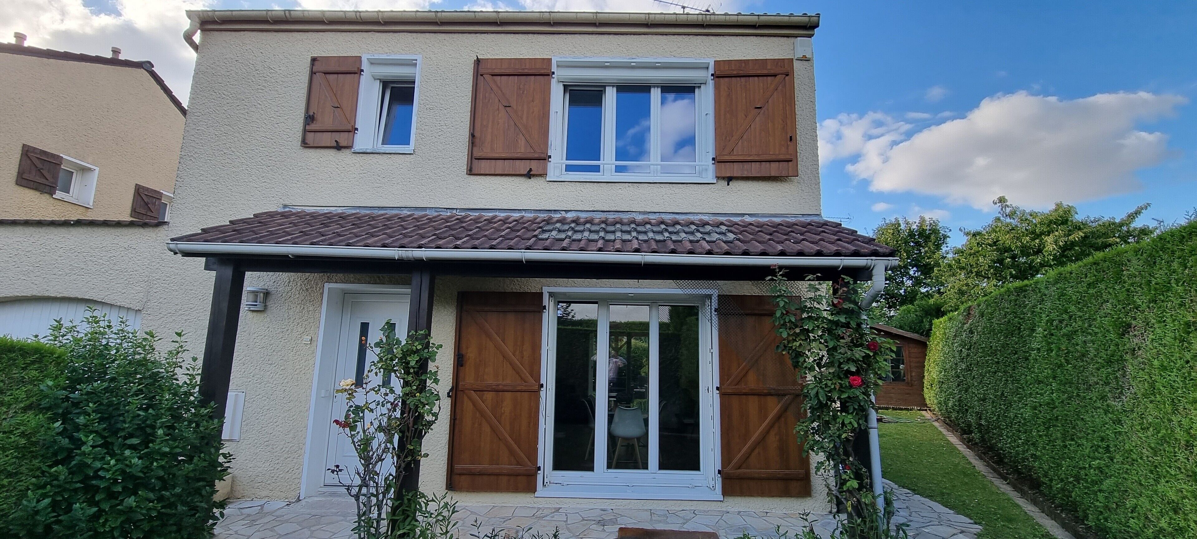 A two-story house with a tiled roof, wooden shutters, and a sliding glass door.