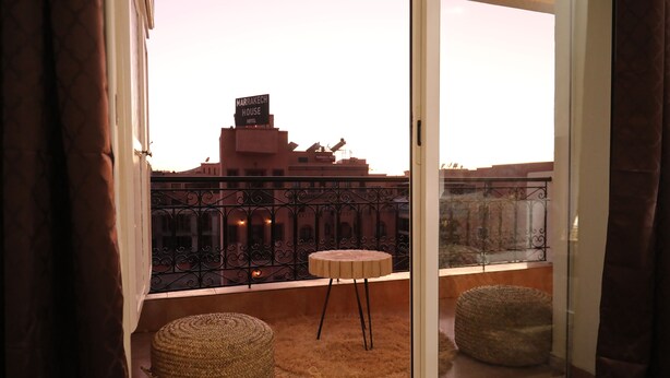 A balcony with a view of the Marrakech House Hotel, featuring a wrought iron railing, a small round table, and two woven ottomans. - SUPERB 2 BED TERRACE APARTMENT GUELIZ MARRAKECH COMFORT&SERVICES AVAILABLE (Marrakech)
