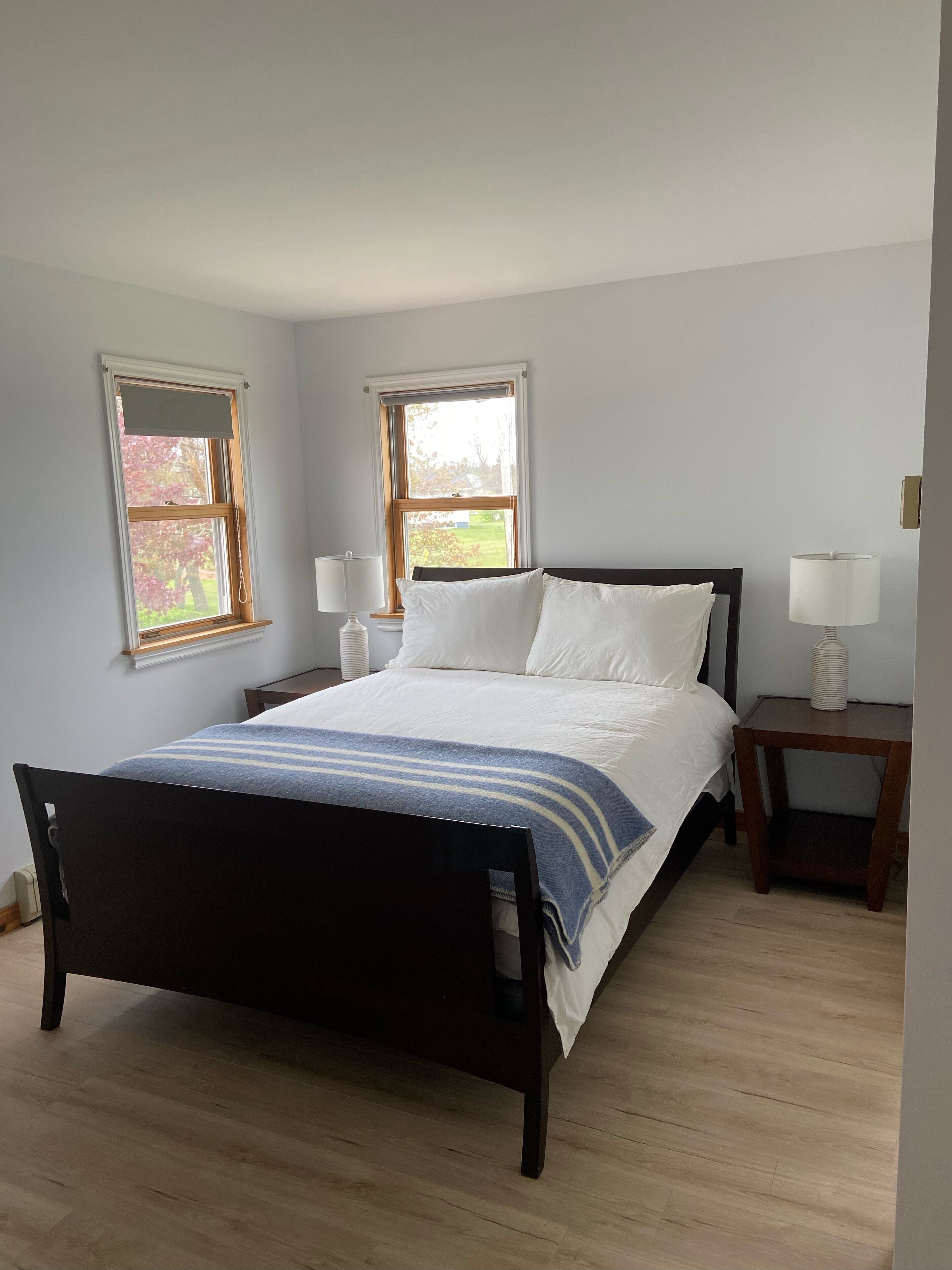 A bedroom with a bed, two bedside tables, and two windows.
