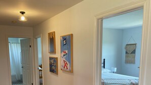 A hallway with wooden flooring leading to a bedroom with a bed and a hanging macrame wall decoration. - Cottage By The Shore (York)