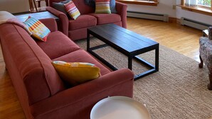A spacious living room with a red sofa, a coffee table, and a dining area with wooden furniture. - Cottage By The Shore (York)