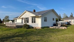 A single-story house with a front porch, a small deck, and a well-maintained lawn. - Cottage By The Shore (York)