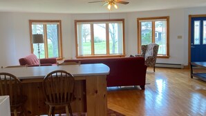 A spacious living room with a wooden dining table, chairs, a red sofa, and a ceiling fan. - Cottage By The Shore (York)