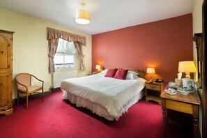 Une chambre à coucher bien rangée, avec un grand lit, une chaise en bois, une table de chevet avec une lampe et une commode.