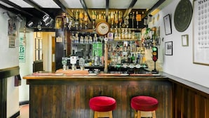 A bar area with wooden stools, a clock, and shelves of bottles. - Queens Head Inn (Harrogate)