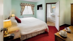 A hotel room with a bed, bedside table with a lamp, a red throw pillow, a wooden nightstand, a telephone, and a magazine on the table. - Queens Head Inn (Harrogate)
