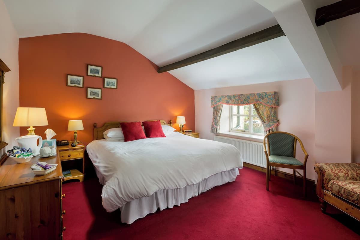 A hotel room with a large bed, two bedside tables with lamps, a wooden dresser, a chair, and a window with curtains.