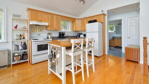 A modern kitchen with wooden cabinets, a central island with bar stools, a refrigerator, and a stove. - Oceanview Cottage on Cabot Trail - Main Level (Englishtown)