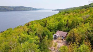 A house surrounded by dense forest with a view of a large body of water. - Oceanview Cottage on Cabot Trail - Main Level (Englishtown)