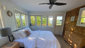 A bedroom with a bed, nightstand, dresser, and a ceiling fan. - Oceanview Cottage on Cabot Trail - Main Level (Englishtown)