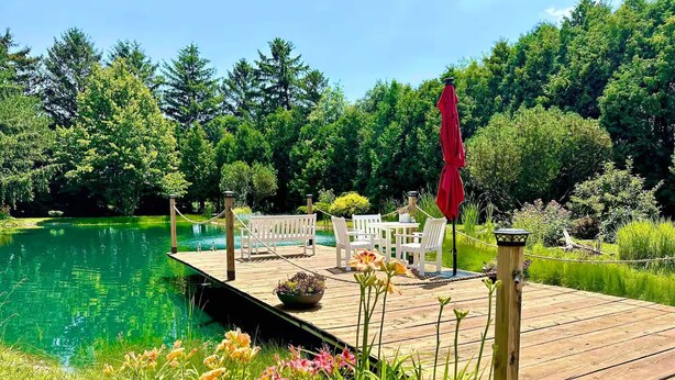 A wooden deck with a pool, surrounded by lush greenery and trees. - The Barn at Bloom & Bower (Risingsun)