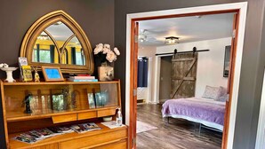 A bedroom with a bed, wooden dresser, mirror, and a door leading to another room. - The Barn at Bloom & Bower (Risingsun)