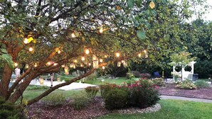 A garden with a tree, string lights, and a white gazebo. - The Barn at Bloom & Bower (Risingsun)