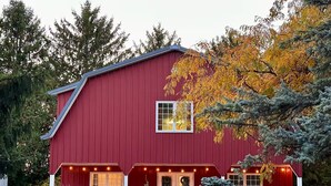 A red barn-style building with a gabled roof, a front porch, and a small window. - The Barn at Bloom & Bower (Risingsun)