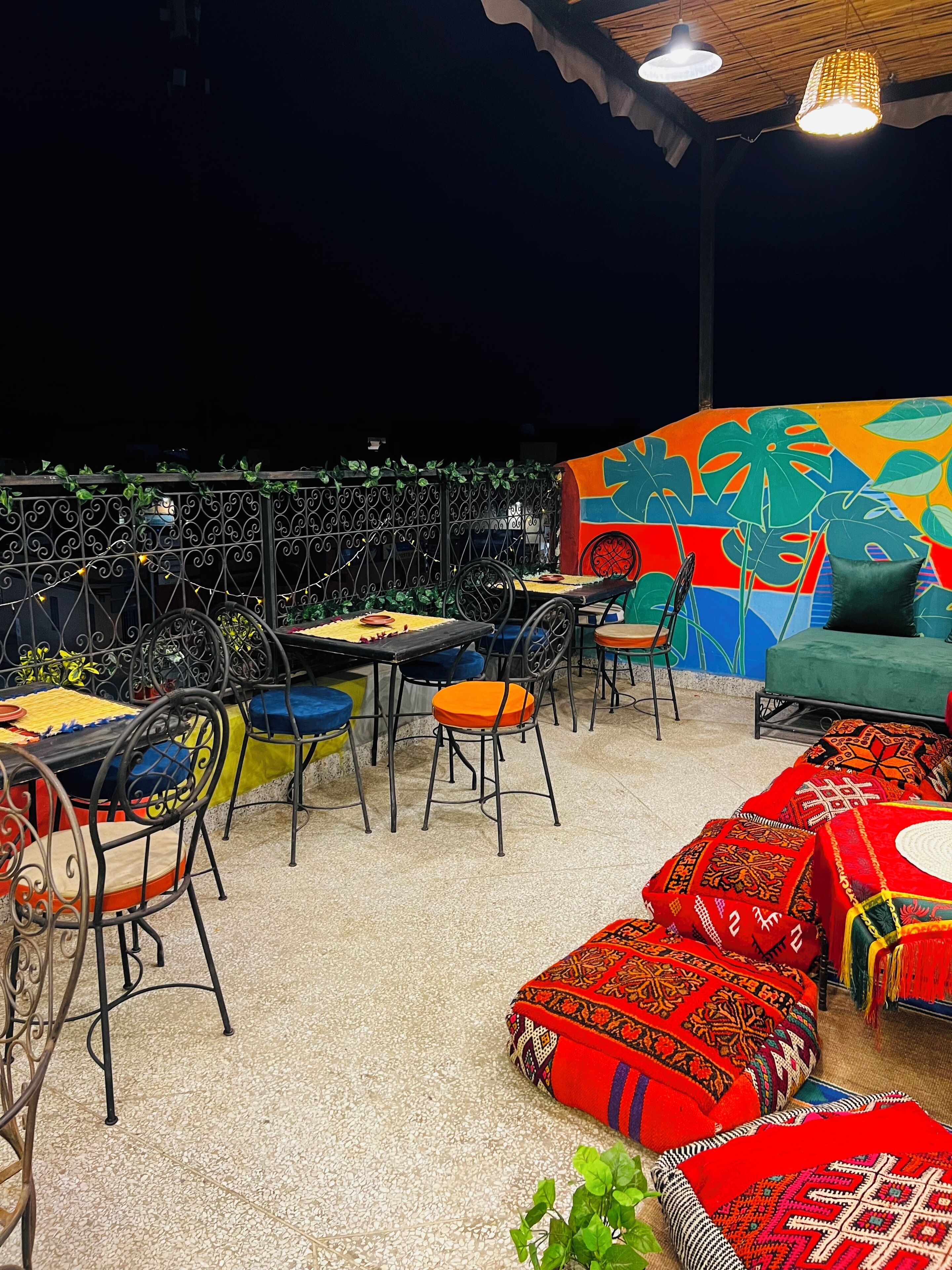 Un espace extérieur aménagé avec des tables et des chaises, une fresque murale colorée et un canapé vert.