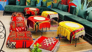 Un espace salon accueillant, avec des canapés verts, des coussins à motifs et une fresque représentant des feuilles tropicales.