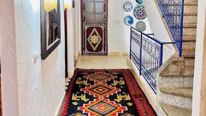 Un couloir avec un tapis à motifs, un escalier avec des rampes bleues et une porte portant l’inscription « Toilettes ».
