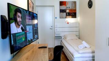 Una habitación pequeña y moderna con un escritorio de madera, una cama, un televisor y un reloj en la pared.