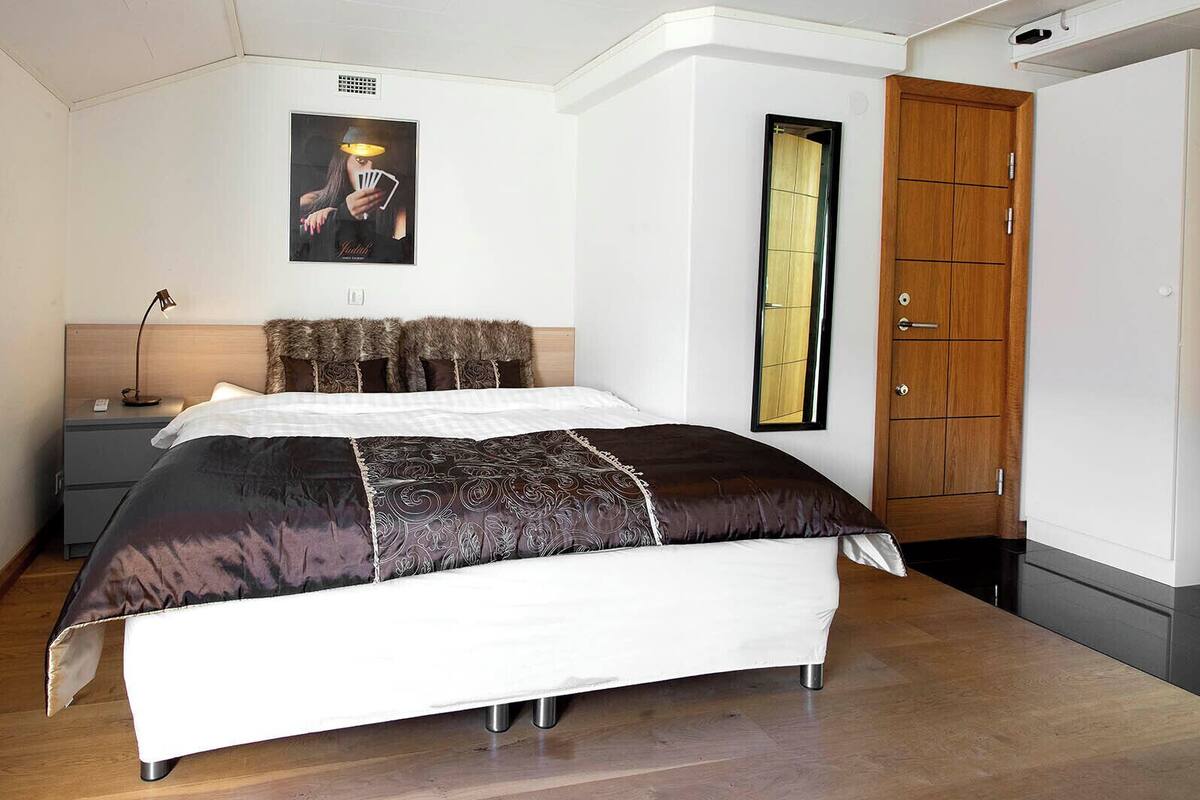 Un dormitorio con cama, mesita de noche, lámpara, armario de madera y dos cuadros en la pared.