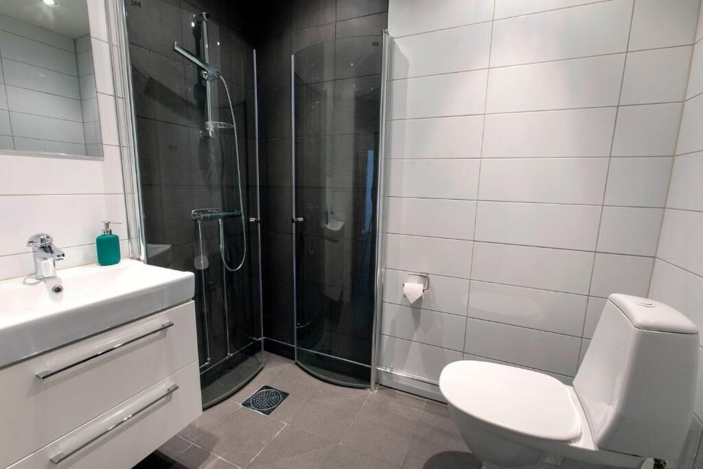 Een moderne badkamer met een glazen douchecabine, een witte wastafel met spiegel en een toilet.
