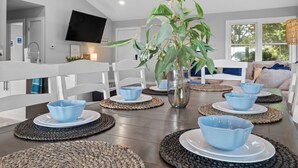 Een moderne eethoek met een houten tafel, afgedekt met blauwe kommen en borden, omringd door geweven tafelonderleggers.