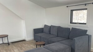 A modern living room with a sectional sofa, a small round table, and a window with a view of trees.