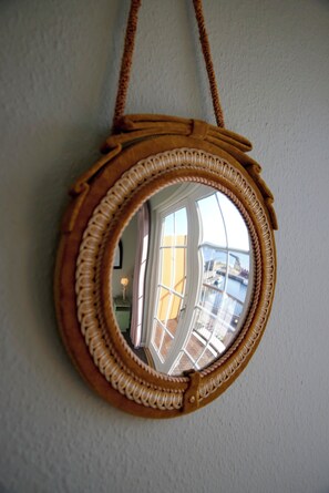 A round mirror with a rope handle, mounted on a wall. - Hotel Kysten (Hasle)