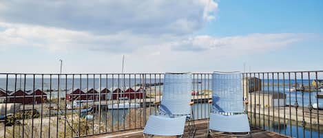 A wooden deck with two striped chairs facing a marina with boats and red buildings in the background.