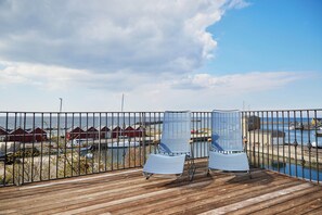 A wooden deck with two striped chairs facing a marina with boats and red buildings in the background. - Hotel Kysten (Hasle)