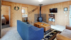 Ein gemütliches Wohnzimmer mit einem blauen Sofa, einem Holztisch, einem Kamin und einem Fernseher auf einem Holzregal.