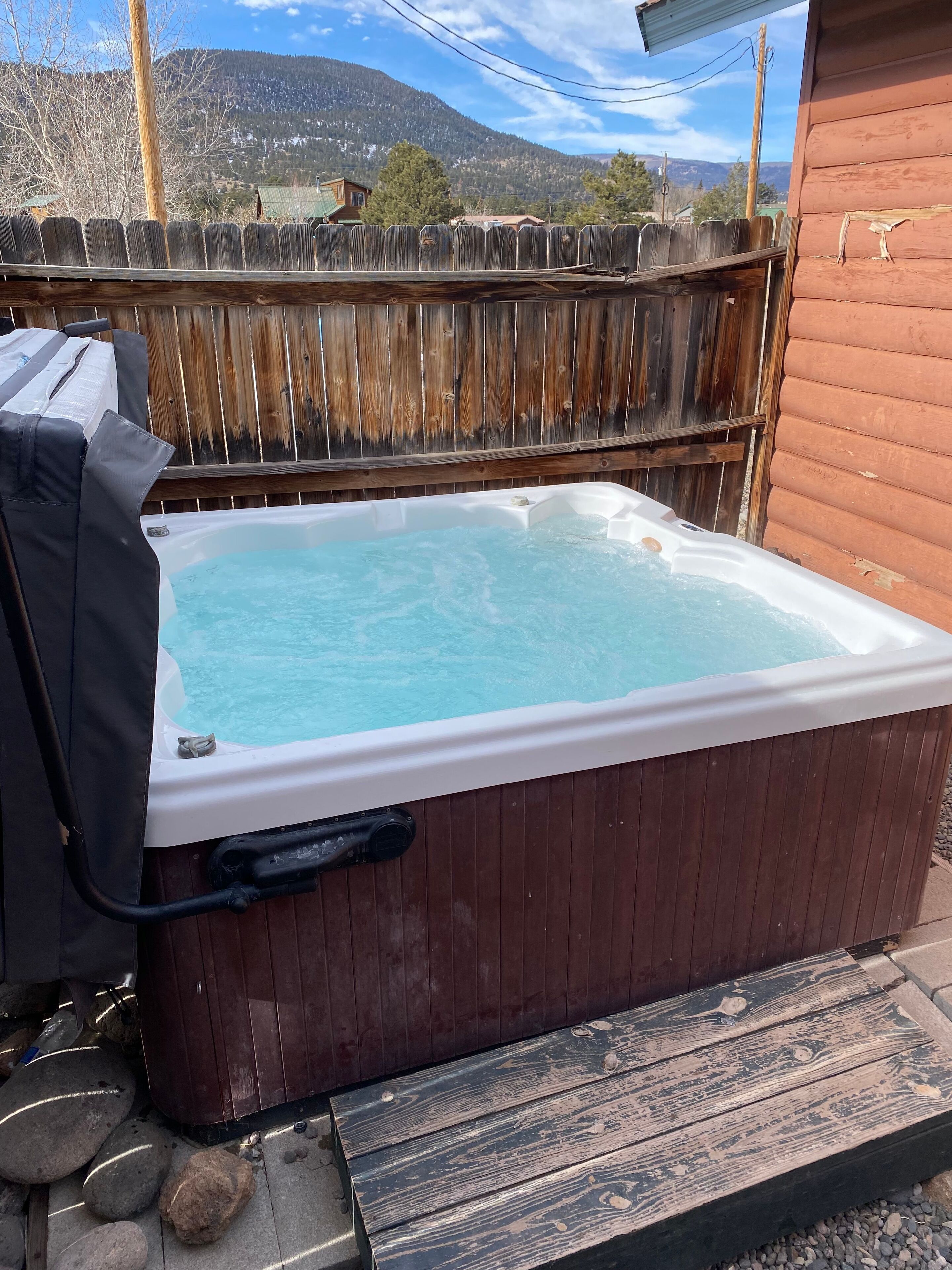 A hot tub in a wooden outdoor setting with a view of mountains in the background.