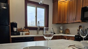 A kitchen with wooden cabinets, a window, a coffee maker, and a bowl on the counter. - Private, Mountain views, Close to Horse Show Grounds, Lake Placid and Hiking (Keene)
