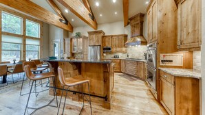 A spacious kitchen with wooden cabinets, a central island, and bar stools. - 6 Bdrm - Caldera Springs: Lodge on the Pond (Bend)