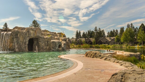 A natural pool with a waterfall, surrounded by rock formations and trees. - 6 Bdrm - Caldera Springs: Lodge on the Pond (Bend)